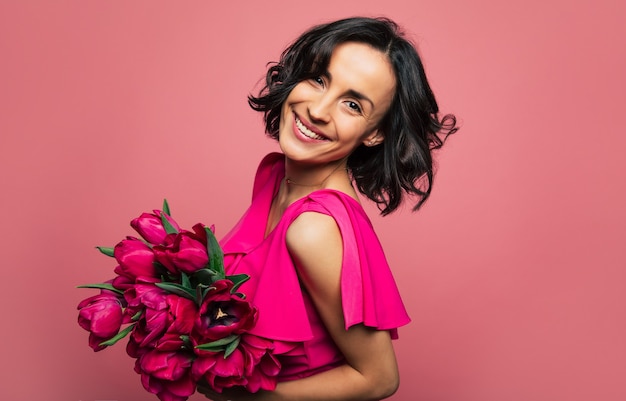 Fiori di primavera. La giovane ragazza splendida in un vestito rosa luminoso sta guardando nella telecamera con un grande sorriso, con in mano un mazzo di tulipani.