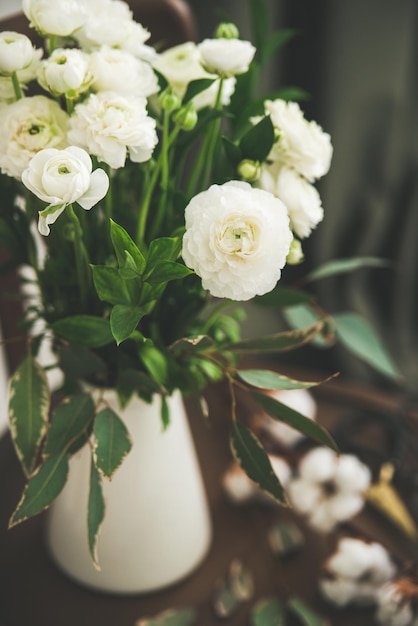 Fiori di ranuncolo bianco primaverile in brocca smaltata con tenda dietro