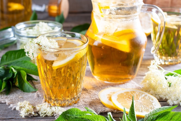 Fiori di sambuco e bevanda al limone. Succo d'estate sano e rinfrescante. Bicchiere di limonata ai fiori di sambuco su tavola rustica in legno. Medicina e terapia alternativa.