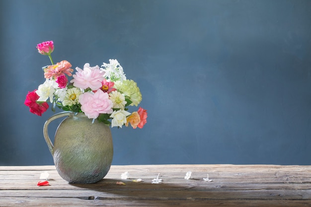 Fiori estivi in brocca di ceramica su tavola di legno su sfondo blu