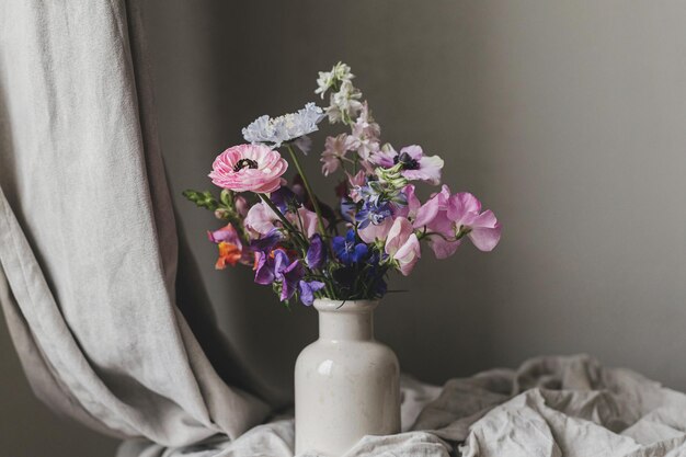 Fiori estivi in vaso natura morta rustica di umore bellissima anemone colorata ranunculus lathyrus scabiosa su panchina invecchiata con panno di lino carta da parati di umore floreale Spazio per testo