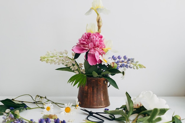 Fiori estivi moderni disposizione di natura morta in vaso vintage su legno bianco Immagine floreale creativa Elegante iris di lupino di peonia e composizione a margherita e forbici su tavolo rustico