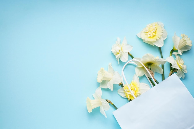 Fiori gialli di narcisi in un sacchetto di carta bianca su uno sfondo azzurro spazio per il testo Vista dall'alto