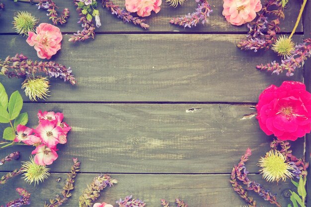 Fiori in cerchio su uno sfondo di legno Cartolina per la vacanza Rose gerani lavanda salvia e castagne pelose sono posti lungo i bordi su tavole scure Spazio copia sfondo piatto