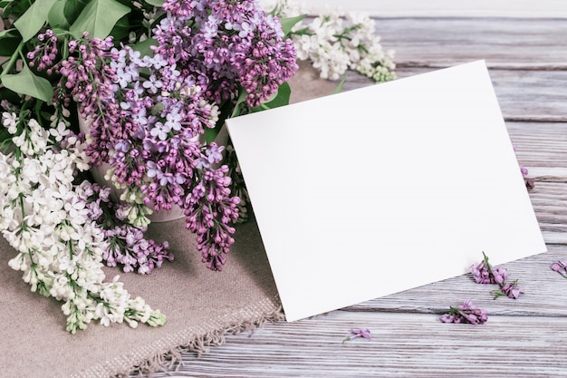 Fiori lilla bianchi e viola con foglio di carta bianco per il testo. Derida sulla carta con il lillà fresco su fondo di legno. Messa a fuoco selettiva.