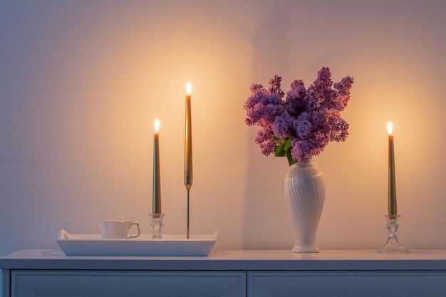 Fiori lilla in vaso bianco e candele dorate su sfondo bianco muro