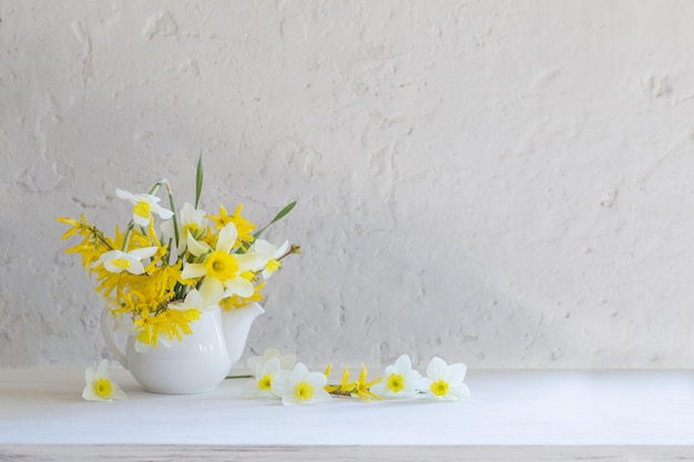 Fiori primaverili bianchi e gialli in vaso su tavola di legno su sfondo bianco