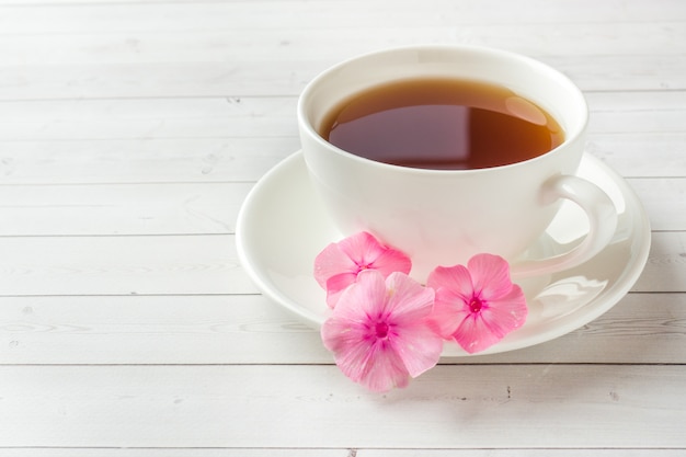 Fiori rosa del flox e una tazza di caffè su una tavola bianca.