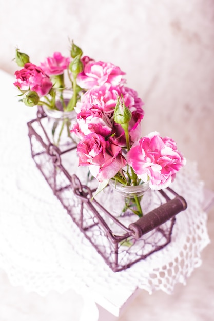 Fiori rosa in bottiglie di vetro in cestino di metallo. Concetto di arredamento vintage