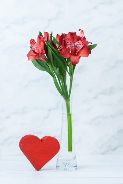 Fiori rossi e un cuore rosso su un fondo di legno bianco. Biglietto di auguri per il 14 febbraio. Close-up con spazio per il testo. Concetto di amore