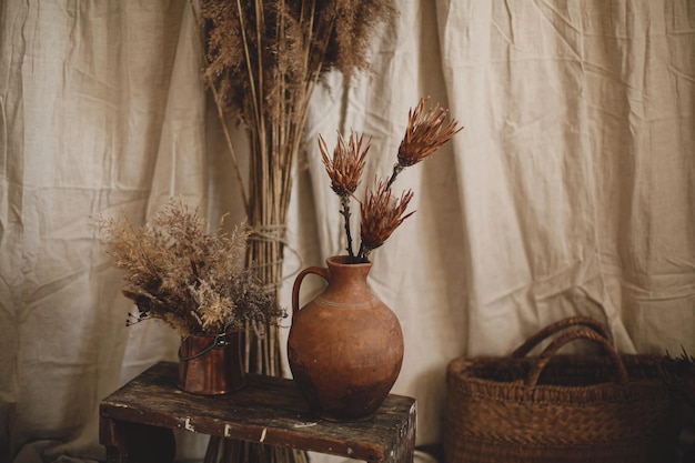 Fiori secchi di protea in vaso di argilla pampas erba cesto di vimini sullo sfondo della stanza boho di stoffa beige