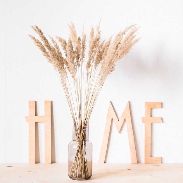 Fiori secchi e lettere di legno a casa sullo sfondo di un muro leggero