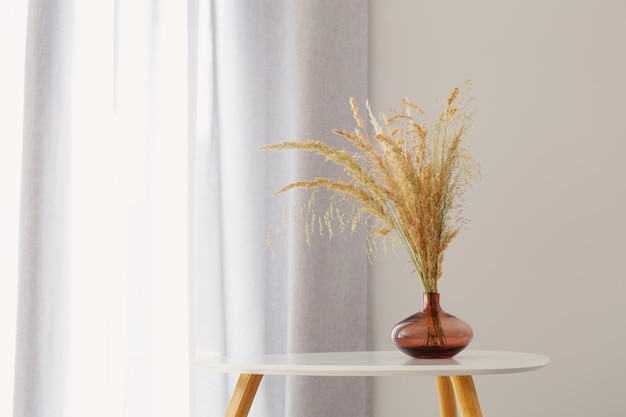 Fiori selvatici secchi in vaso di vetro in interno grigio