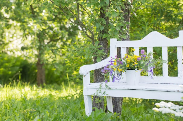 Fiori selvatici sulla panca in legno bianco nel giardino estivo