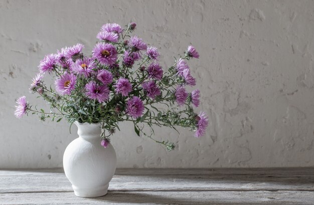 Fiori viola in vaso bianco sulla vecchia parete