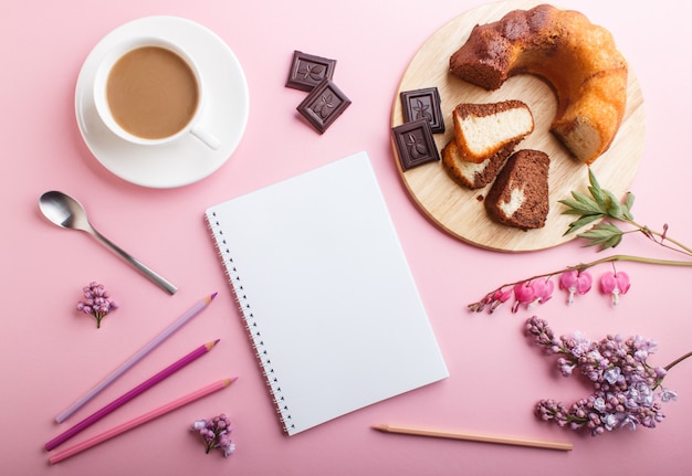 Fiori viola lilla e sanguinante cuore e una tazza di caffè con notebook, torta e matite colorate