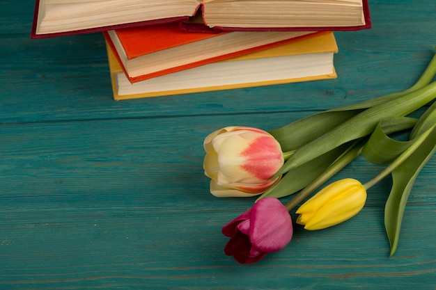 Fiorisce tulipani e libri su un tavolo di legno blu