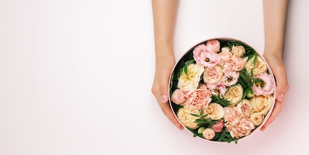 Fiorista che tiene una scatola rotonda del cappello con la composizione floreale su un fondo rosa con lo spazio della copia. Confezione regalo per l'8 marzo, San Valentino, festa della mamma, compleanno. nozze.