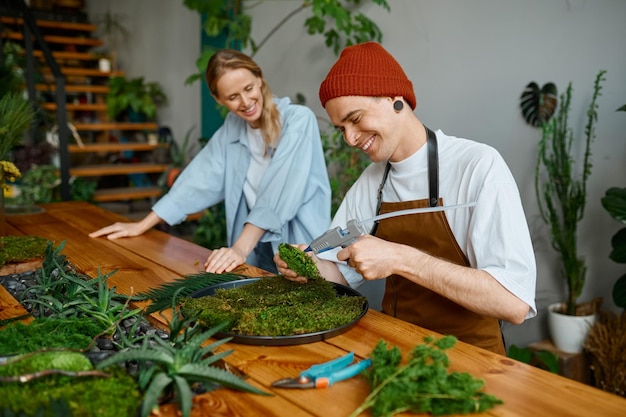 Fiorista donna che insegna al giovane decoratore uomo hipster come comporre un pezzo di muschio sul piatto al laboratorio di studio di artigianato artistico