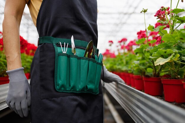 Fiorista donna in grembiule e cintura con tasche per attrezzi da giardino nella serra