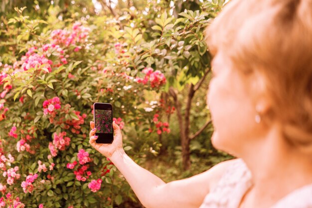 Fiorista donna scatta una foto di fiori sul suo telefono in giardino