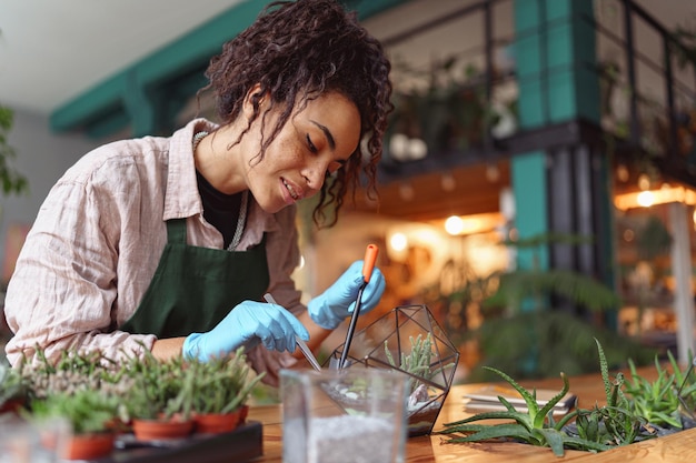 Fiorista donna sorridente professionista che fa composizione di piante succulente nello studio di disegno floreale