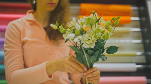 Fiorista femmina fa mazzo di fiori lei taglia la carta da imballaggio lavorando nel negozio di fiori Carino giovane professionista caucasico fa bouquet in vendita nel negozio di fiori Fiorai fatti a mano piccola impresa