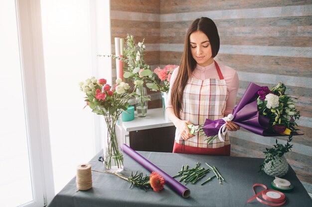 Fiorista femminile al lavoro: bella giovane donna dai capelli scuri che fa moda bouquet moderno di fiori diversi. Donne che lavorano con i fiori in officina