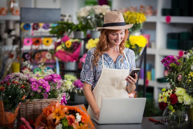 Fiorista femminile che per mezzo del telefono cellulare mentre per mezzo del computer portatile