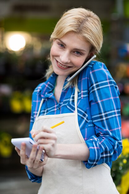 Fiorista femminile che prende ordine sul telefono cellulare nel negozio di fiore