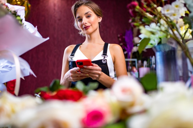 Fiorista femminile in piedi al bancone del suo negozio di fiori tramite la consegna del telefono cellulare