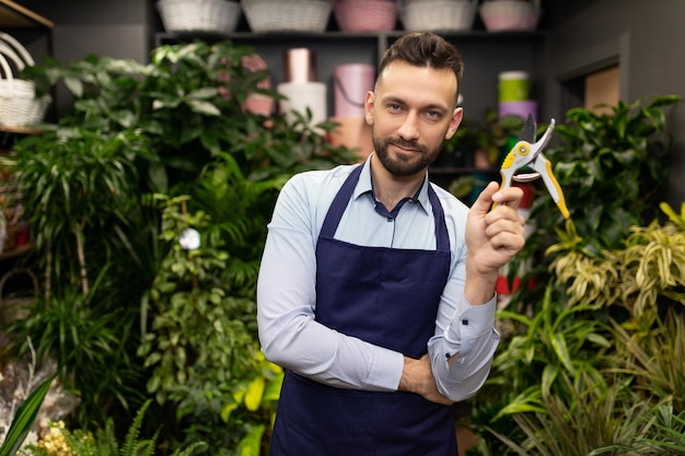 Fiorista giardiniere di successo si trova in un negozio di fiori con un potatore in mano e guarda con a