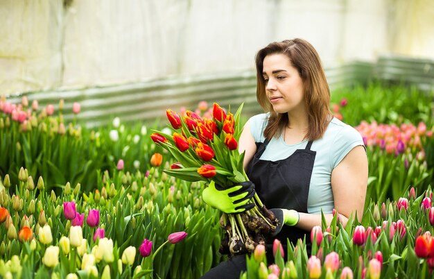 Fiorista giardiniere donna sorridente che tiene un mazzo di fiori in piedi in una serra dove coltivano i tulipani