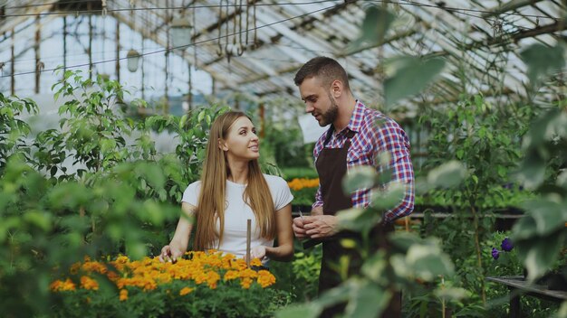 Fiorista giovane uomo allegro che parla con il cliente e dà consigli mentre lavora nel centro di giardinaggio