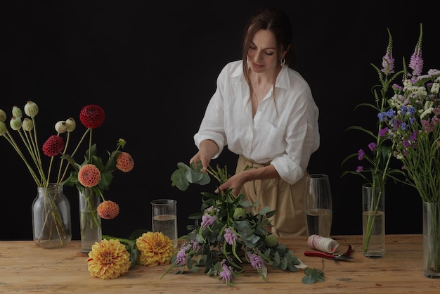 Fiorista ragazza raccoglie un bouquet in un laboratorio di fiori su un layout di sfondo scuro per la floristica