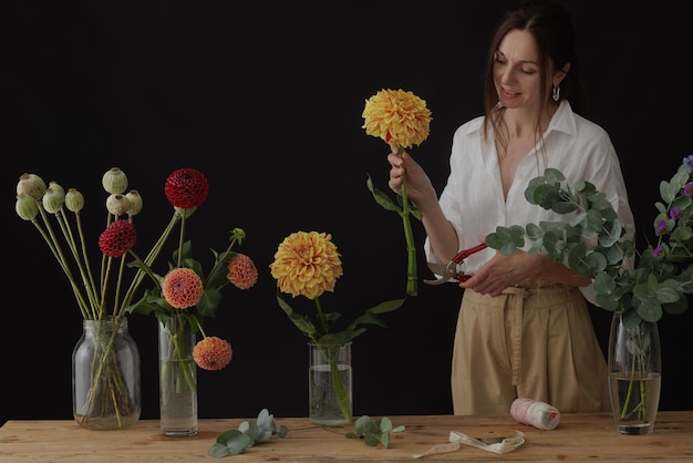 Fiorista ragazza raccoglie un bouquet in un laboratorio di fiori su un layout di sfondo scuro per la floristica