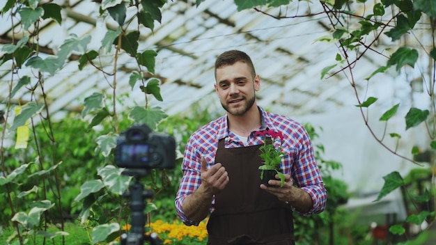 Fiorista uomo giovane blogger sorridente in grembiule con fiore che parla e registra video blog