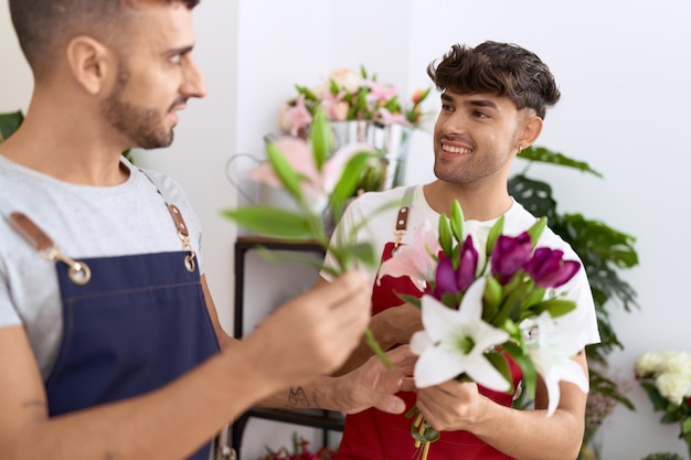 Fioristi di due uomini ispanici che sorridono fiduciosi che tengono il mazzo dei fiori al negozio di fiori