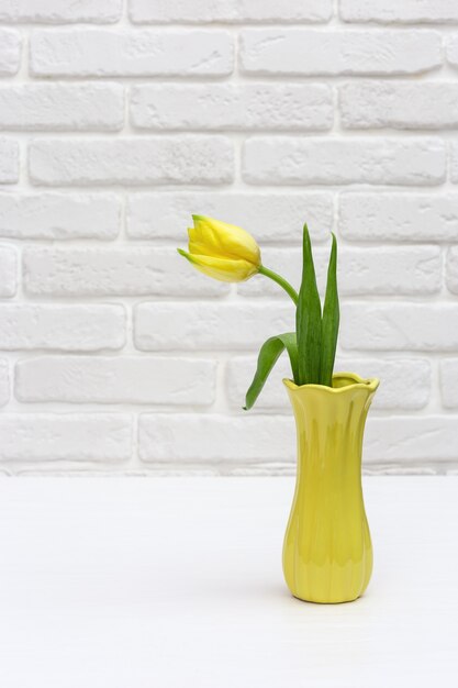 Fioritura di fiori di tulipano in piccolo vaso giallo sul muro di mattoni bianchi in camera. Bouquet di fiori come regalo di primavera per la festa della donna o della mamma. Formato verticale.