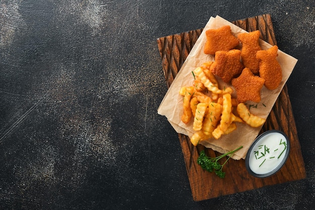 Fish and Chips fast food britannico Bastoncini di pesce con patatine fritte adagiati su tavola rustica su sfondo di cemento vecchio scuro Tradizionale cibo di strada autentico britannico o cibo da asporto Mock up Vista dall'alto