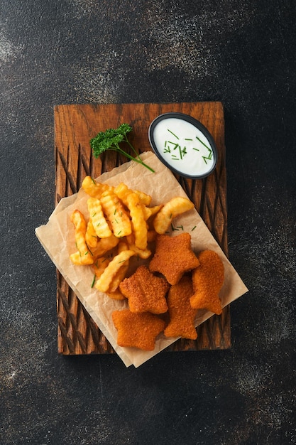 Fish and Chips fast food britannico Bastoncini di pesce con patatine fritte adagiati su tavola rustica su sfondo di cemento vecchio scuro Tradizionale cibo di strada autentico britannico o cibo da asporto Mock up Vista dall'alto