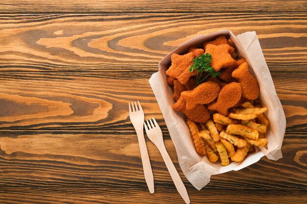 Fish and Chips fast food britannico Bastoncini di pesce con patatine fritte su piatto di carta da asporto su sfondo vecchio tavolo in legno Tradizionale cibo di strada autentico britannico o cibo da asporto Mock up