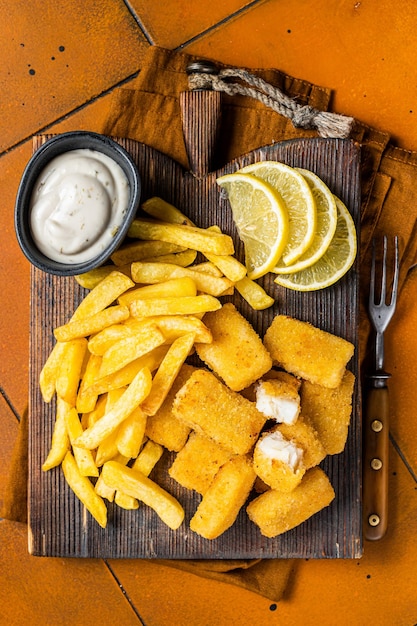 Fish and Chips Fastfood britannico Bastoncini di pesce con patatine fritte su tavola di legno Sfondo arancione Vista dall'alto