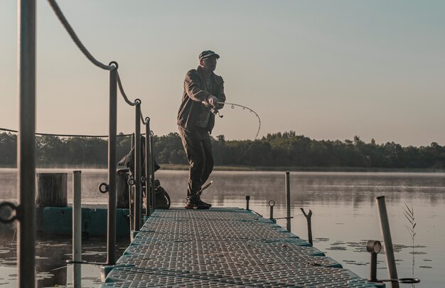 Fisher pesca in mattinata nebbiosa uomo con canna da pesca in appoggio sul lago nella nebbia