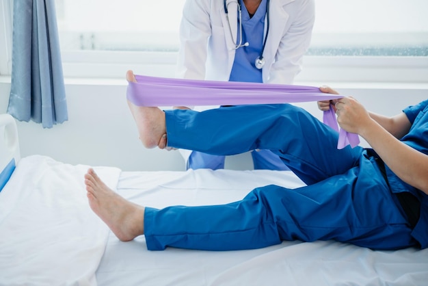 Fisioterapista che aiuta il paziente mentre allunga la gamba a letto in clinica xA