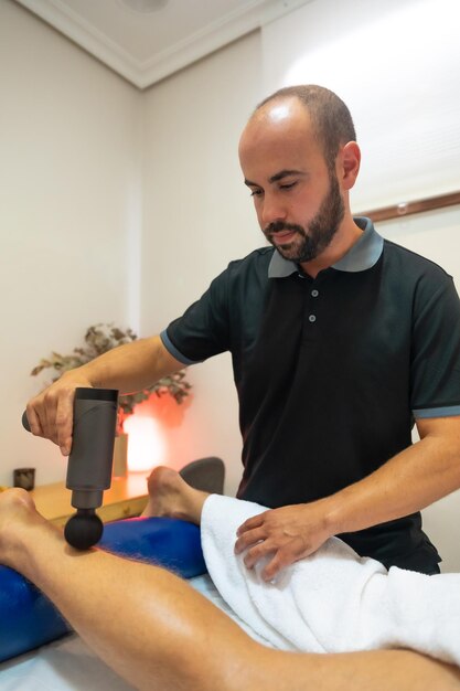 Fisioterapista che fa un massaggio fisioterapico al cliente sulla palla della gamba con una macchina