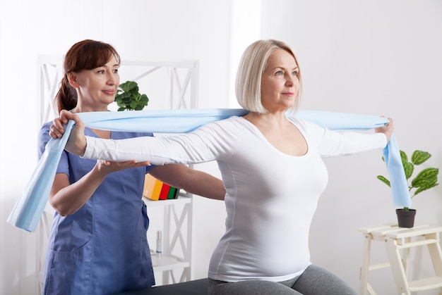 Fisioterapista e donna che si siedono su un letto che si esercita con un nastro di gomma
