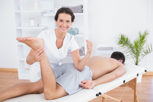 Fisioterapista facendo massaggio alle gambe e sorridere alla telecamera
