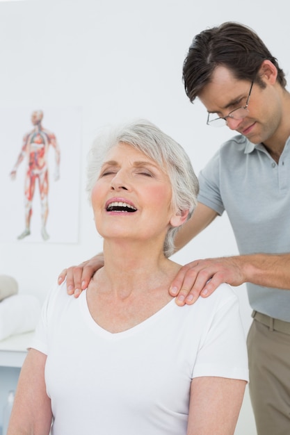 Fisioterapista maschio che massaggia le spalle di una donna senior