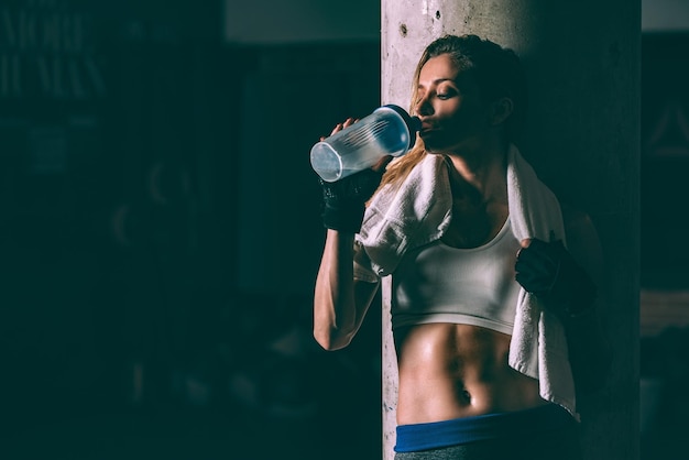 Fit bionda donna stanca che riposa e beve dopo l'allenamento allenandosi in palestra